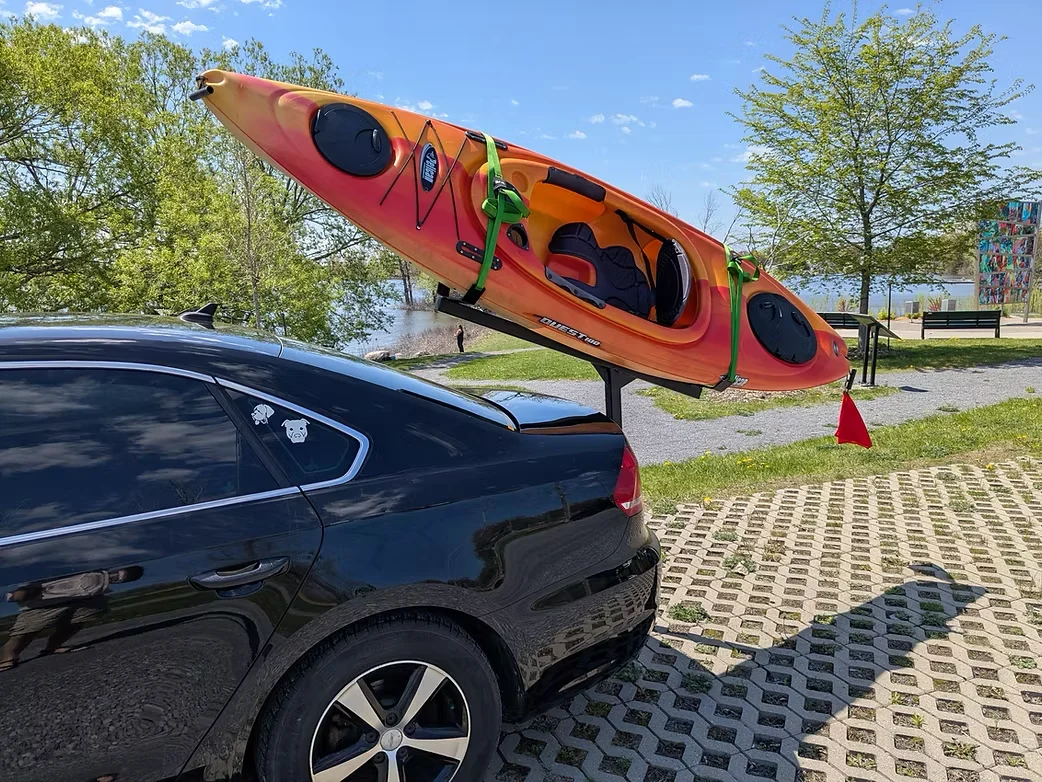 Orange kayak carried behind a black sedan using the Kayak Hitch Rack